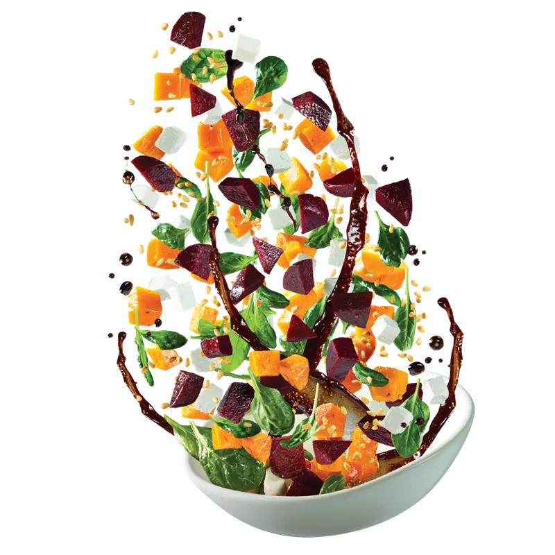 Pumpkin, beetroot, feta and spinach salad tossed mid-air above a white bowl