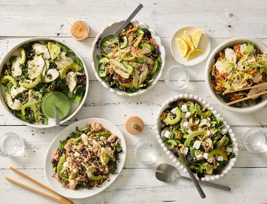 A table of fresh Salad Servers bowls with chicken, avocado, tuna and feta