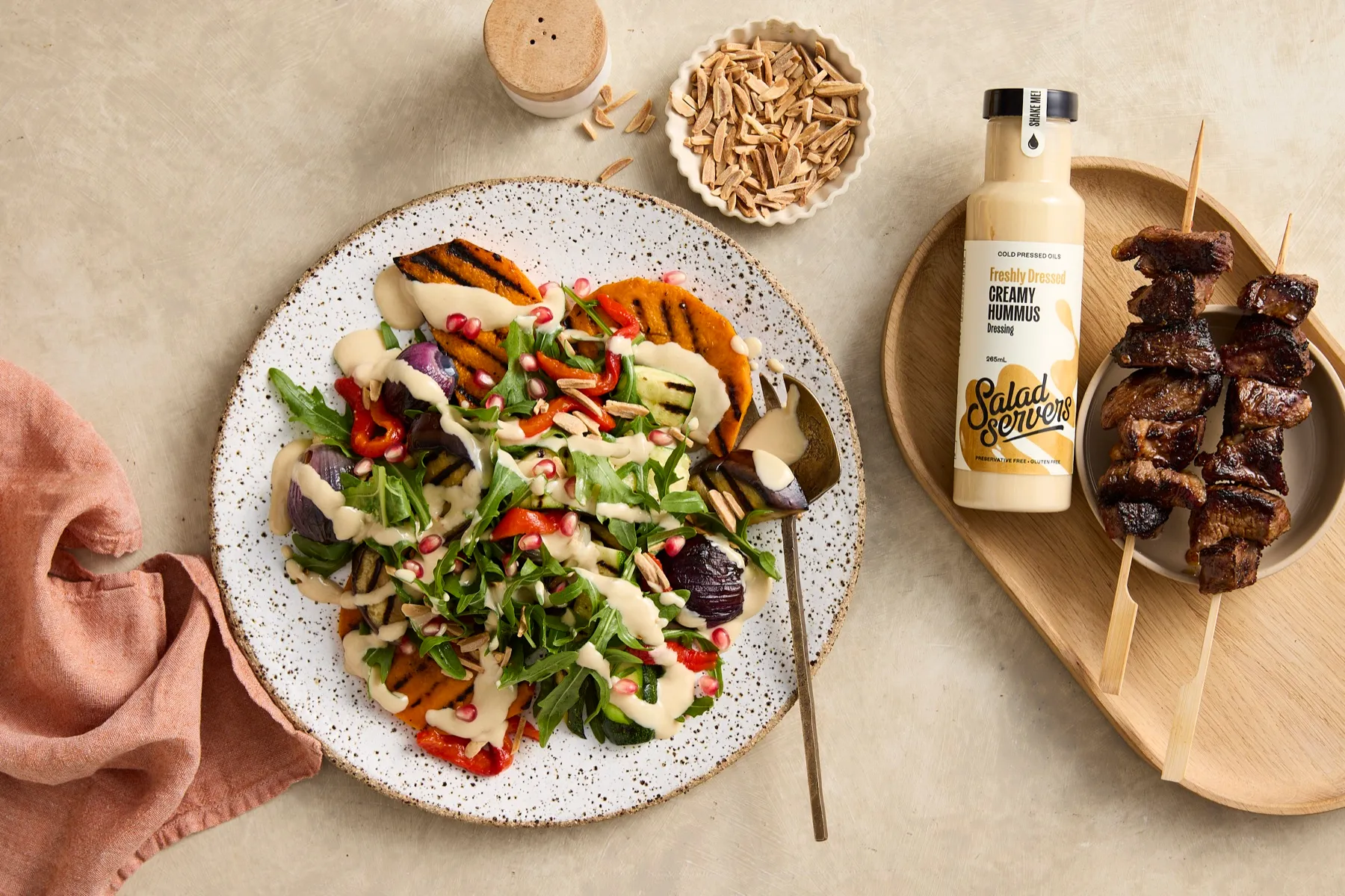 Roasted vegetable salad with rocket, pomegranate and almonds drizzled with Salad Servers Creamy Hummus dressing, with grilled lamb skewers on the side