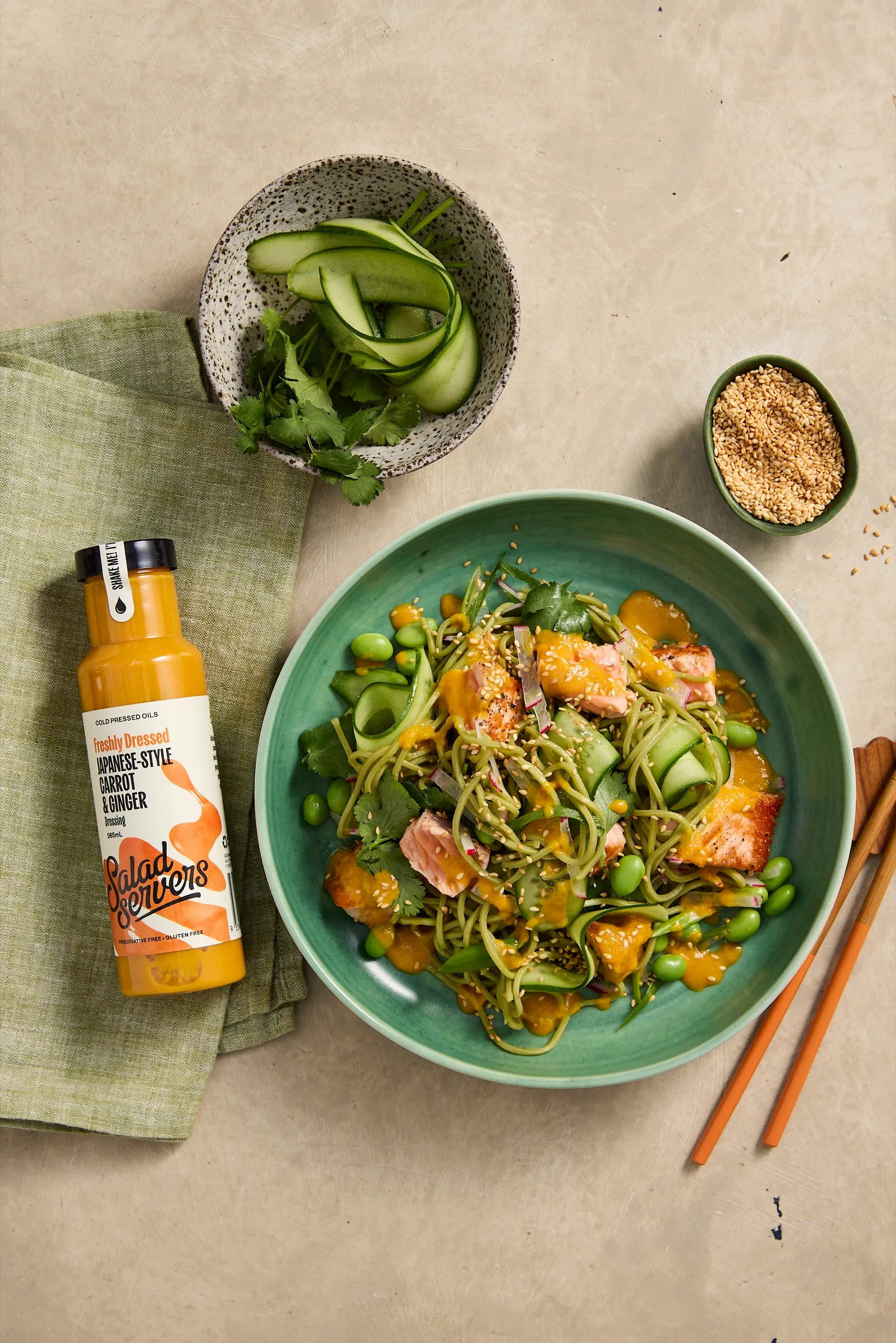 Green tea soba noodles with flaked salmon, edamame and cucumber in a green bowl, dressed in Salad Servers Japanese-Style Carrot and Ginger dressing
